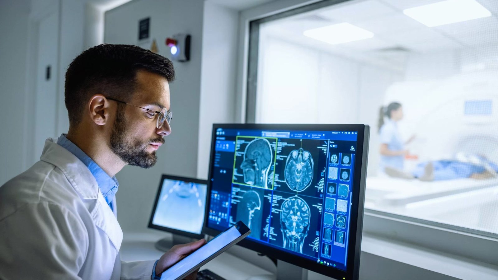 A man in a lab coat examines data on a computer screen in a laboratory setting.