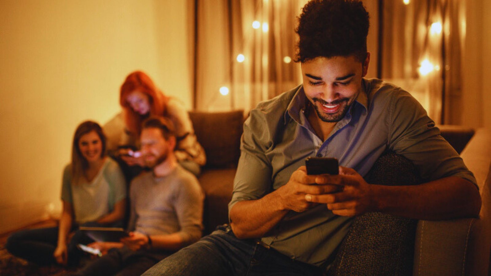 A man comfortably seated on a couch, using his phone while looking relaxed.