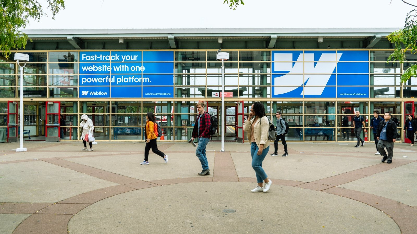 A group of people walking in front of a large, modern building with glass windows and a clear blue sky above.