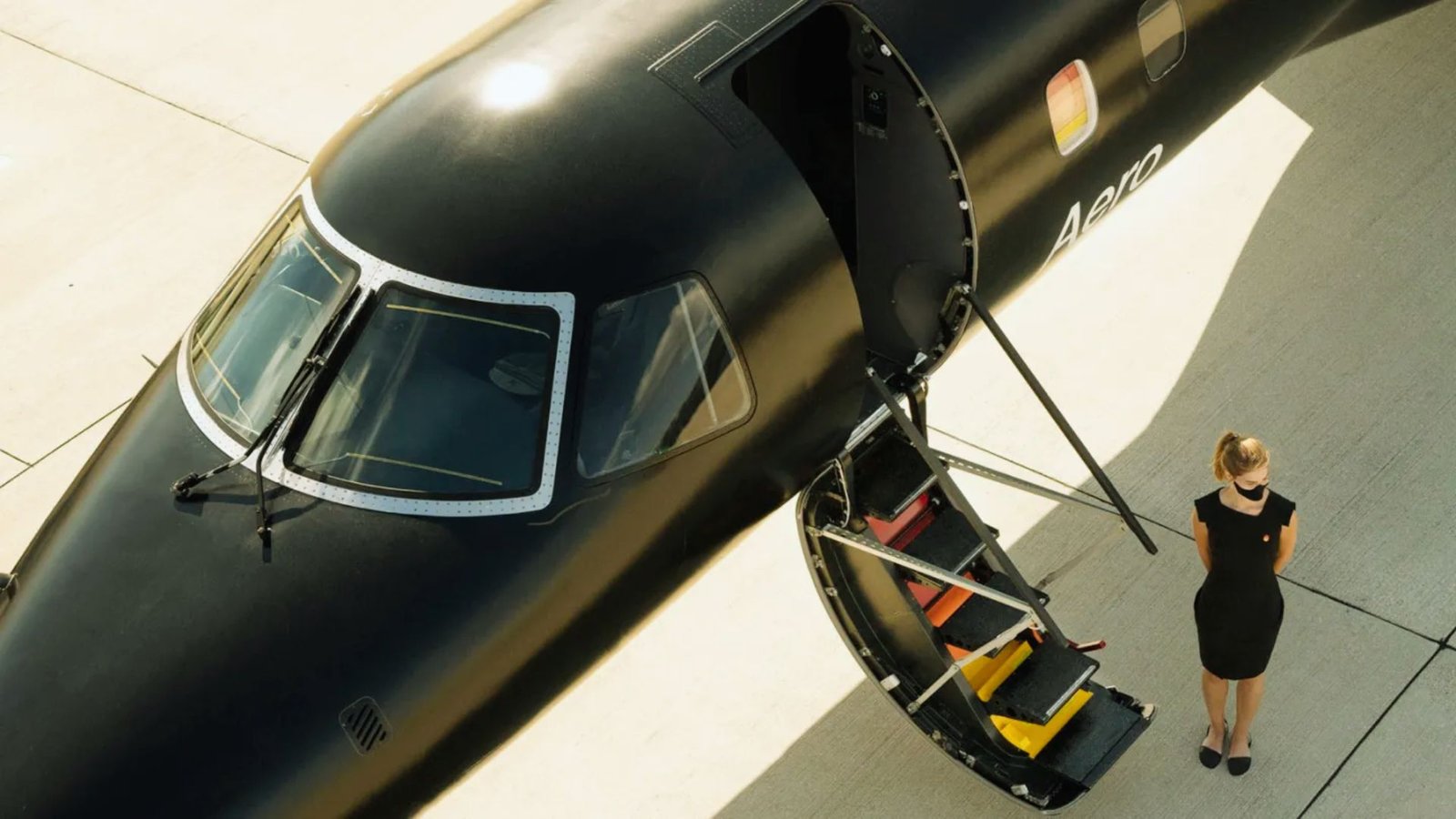 A woman stands beside a sleek black airplane, smiling as she poses for the photo.