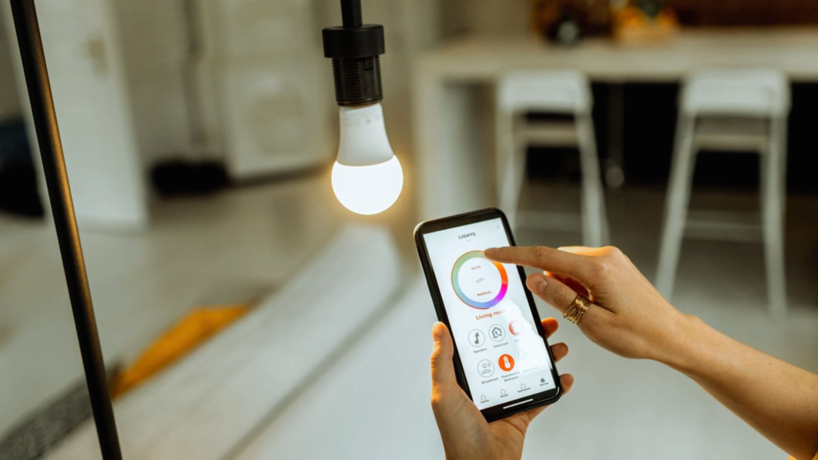 A person using a smartphone to adjust the brightness of a smart light bulb in a modern living space.