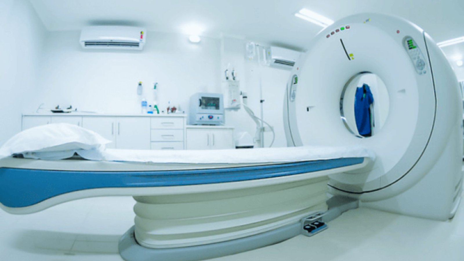 MRI machine positioned in a hospital room, ready for patient use, with medical equipment and soft lighting surrounding it.
