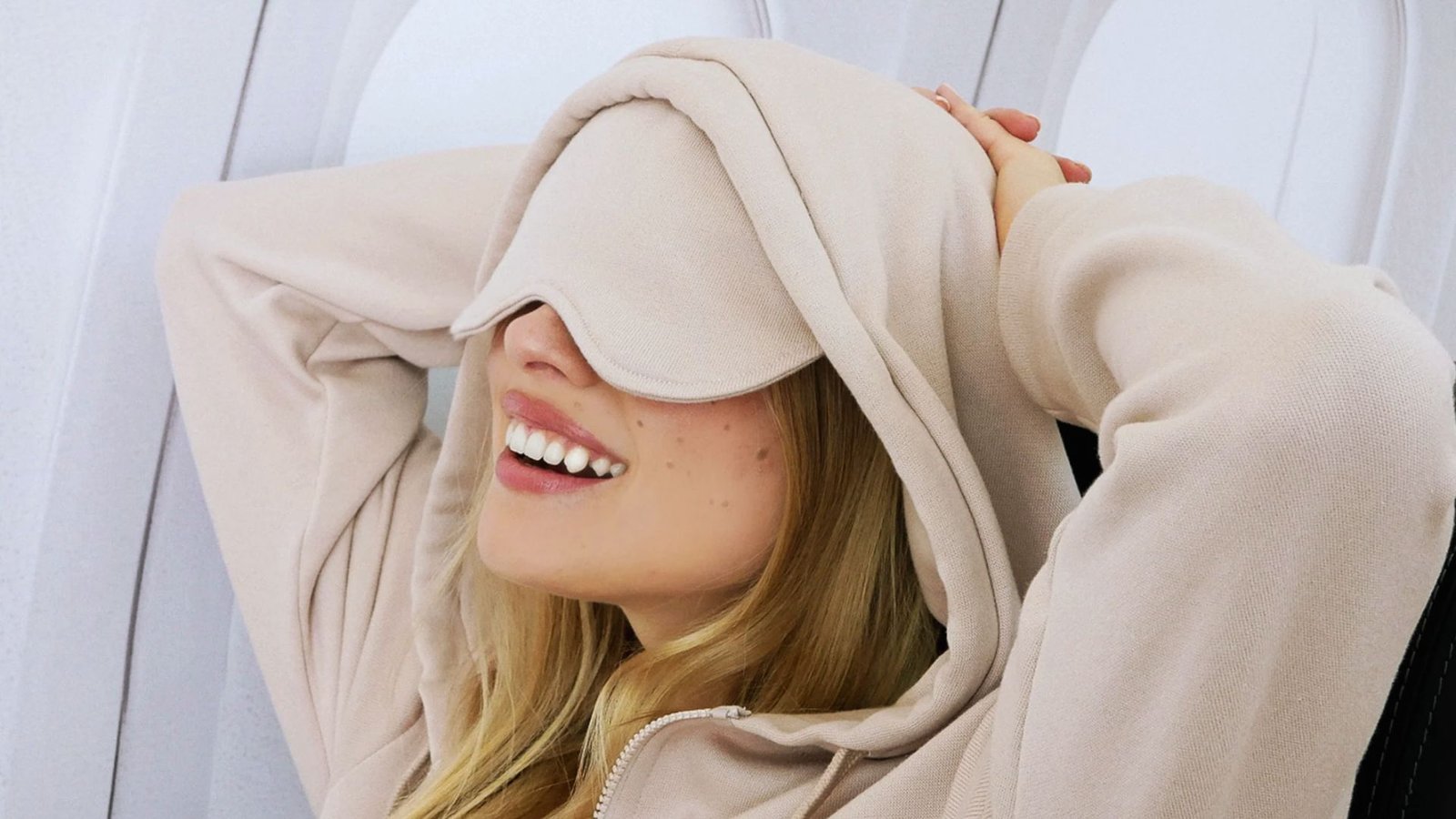  A woman in a hoodie and sunglasses sits on an airplane, looking relaxed and ready for her journey.