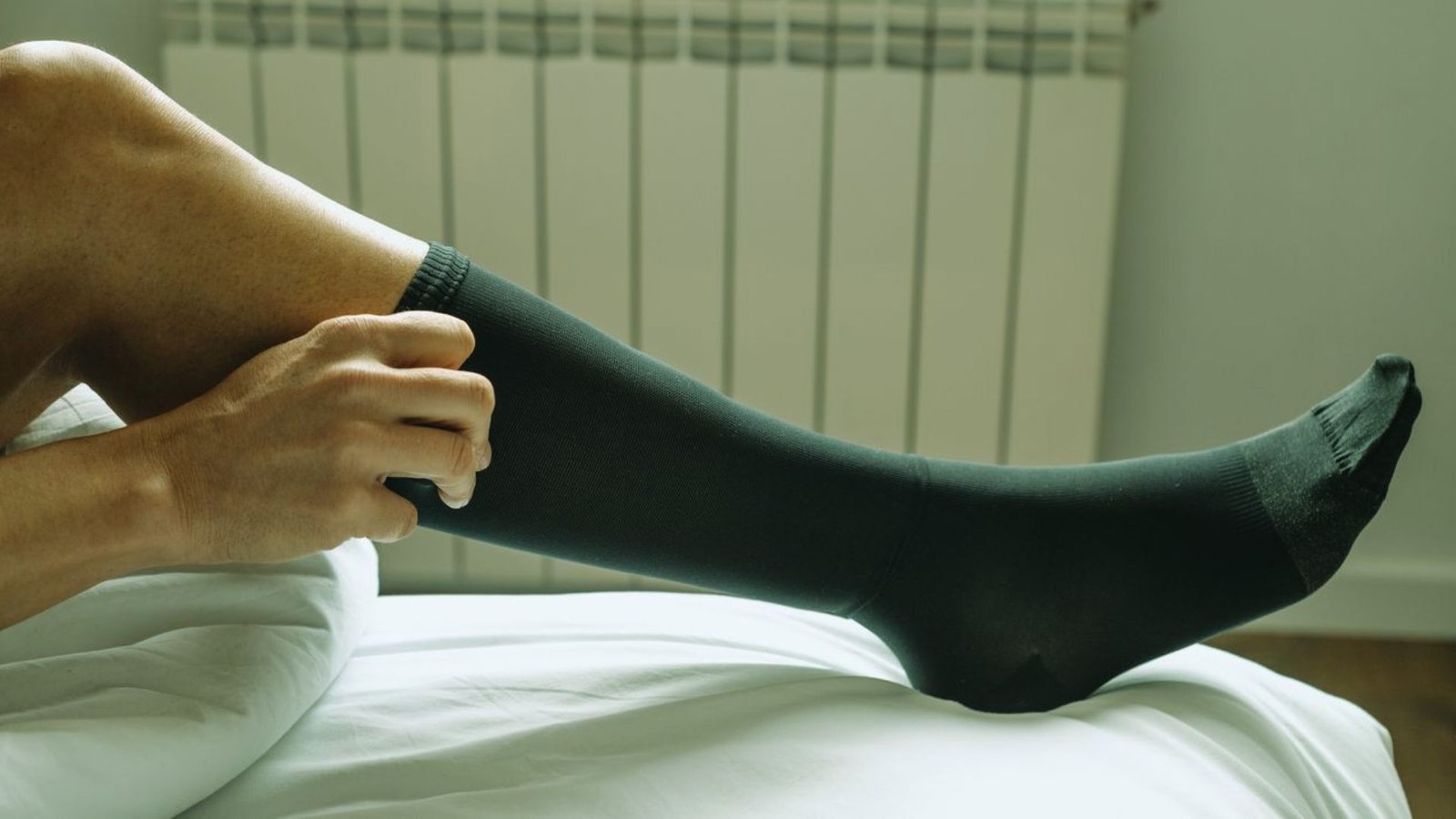 A man is sitting down, putting on his socks with a focused expression on his face.