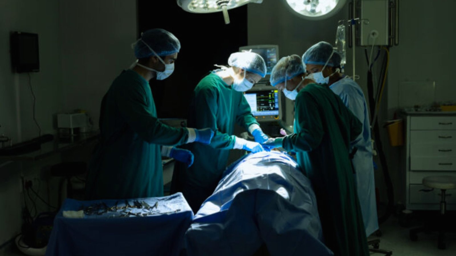  Surgeons in an operating room, wearing masks and gloves, work together on a surgical procedure with various instruments nearby.