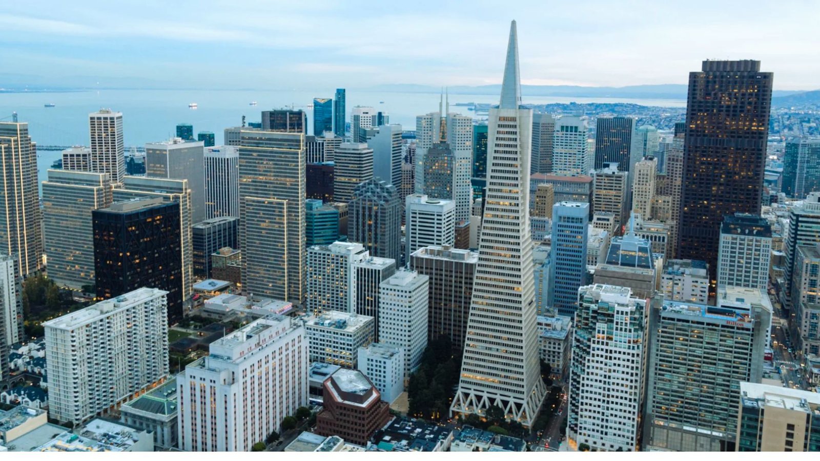 Aerial view of the San Francisco skyline, showcasing iconic buildings and the Golden Gate Bridge in the background.