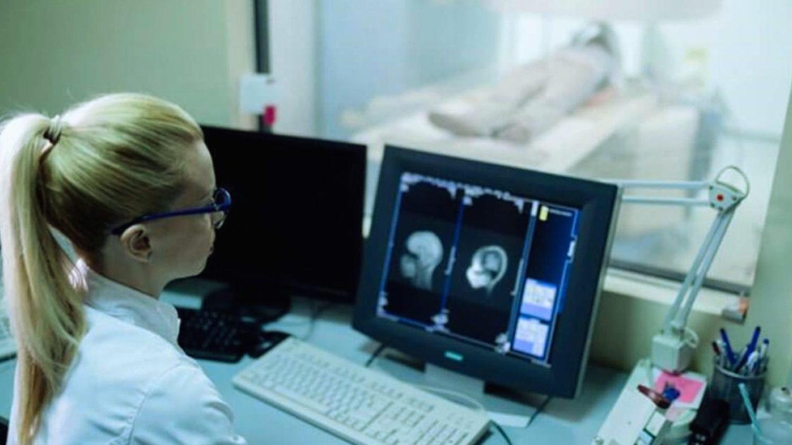 A woman in a white lab coat examines data on a computer screen in a laboratory setting.