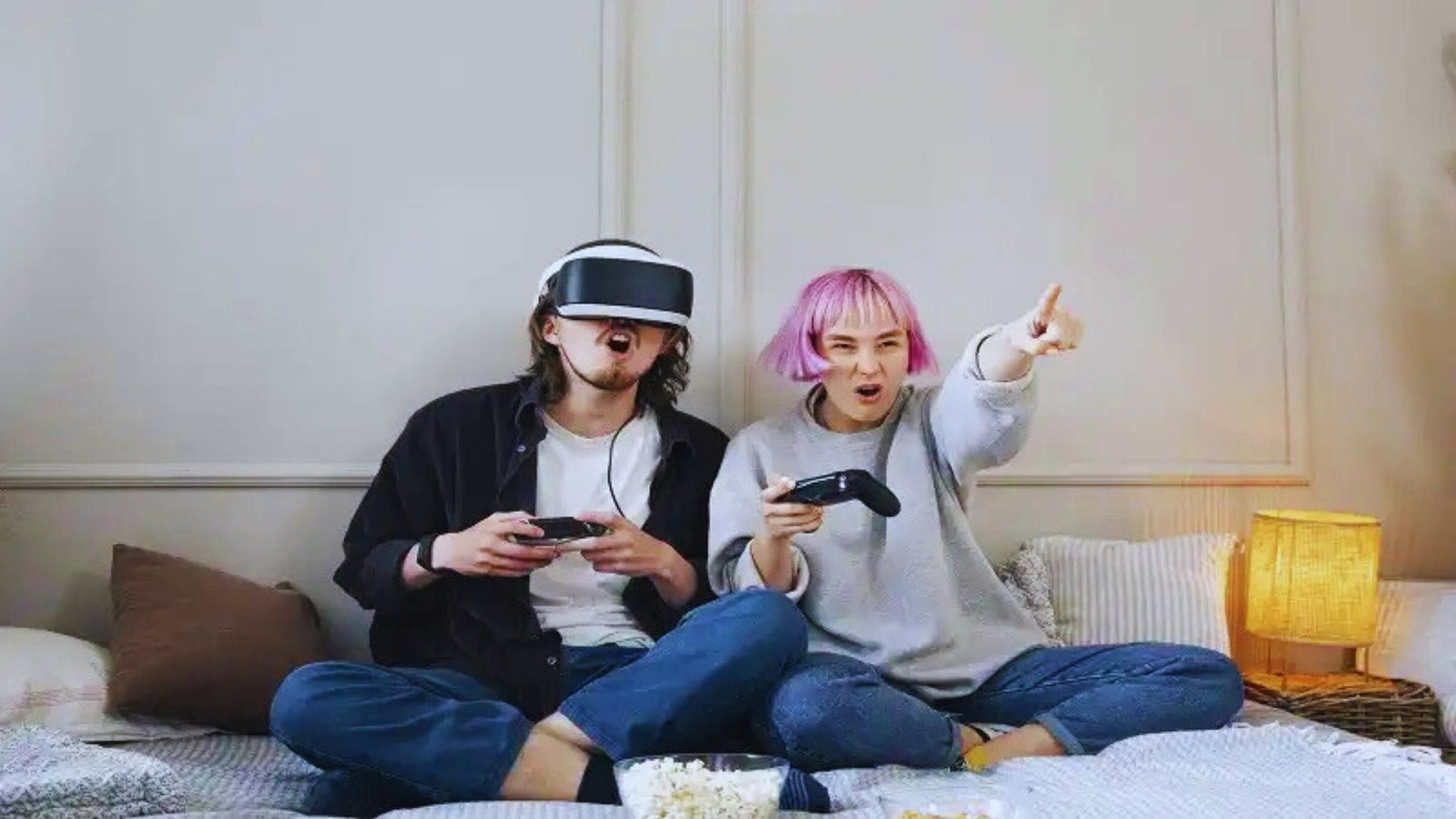 A couple wearing virtual reality glasses sits on a bed, engaged in an immersive digital experience together.