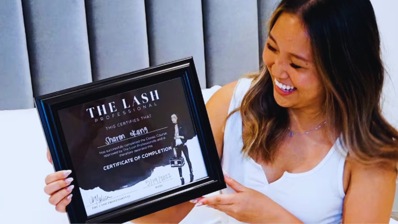 A woman proudly holds a framed certificate, smiling as she showcases her achievement.