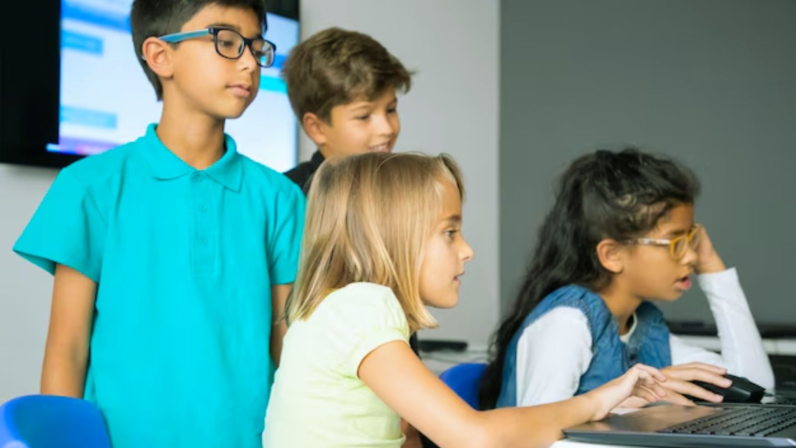 Children engaged with computers in a bright classroom, focused on their screens and collaborating on projects.