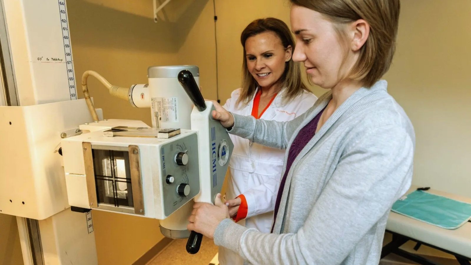  Two women in lab coats examining a scientific machine in a laboratory setting.
