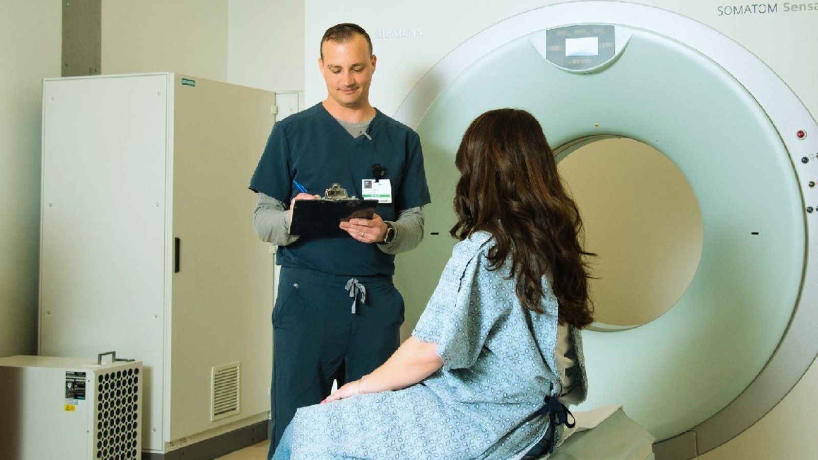 A man and woman stand together in front of an MRI machine, discussing the procedure with a focused expression.
