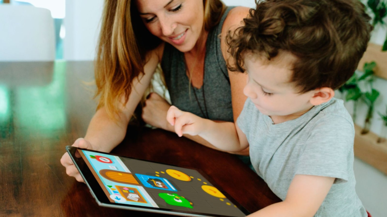 A woman and a child joyfully playing together with an iPad, engaging in a fun and interactive activity.