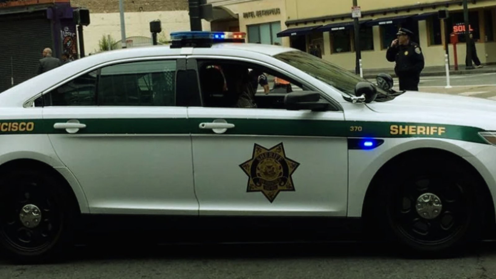 A parked sheriff's car along the roadside, with a view of the landscape and blue sky above.