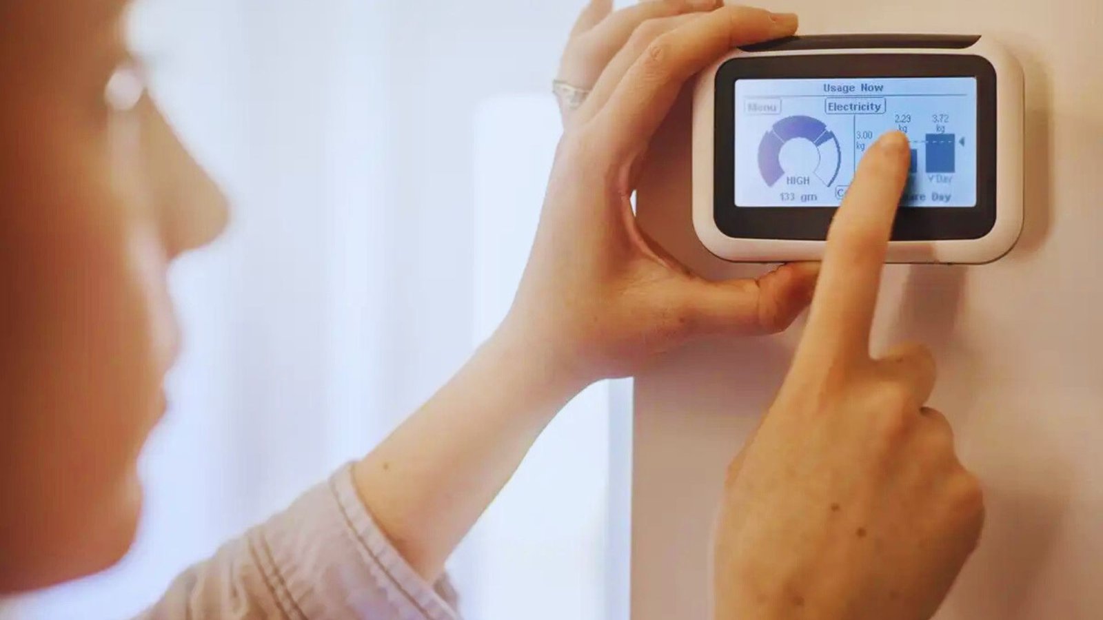  A woman interacts with a smart thermostat, touching its screen to change the temperature settings.
