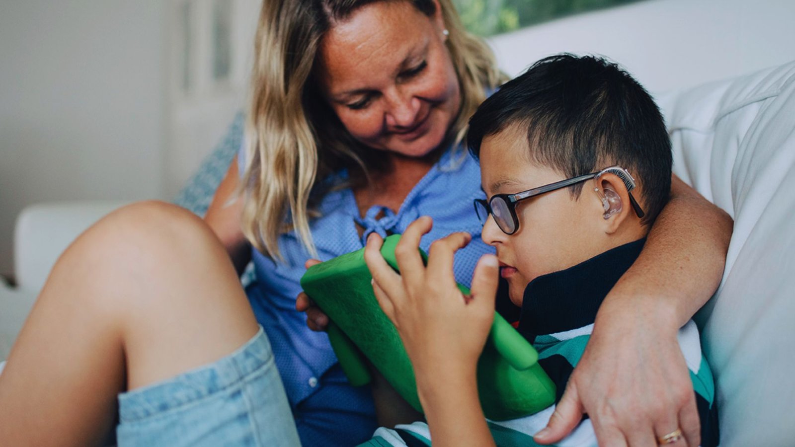 A woman and a boy sit together on a couch, engaging with a tablet in a cozy living room setting.