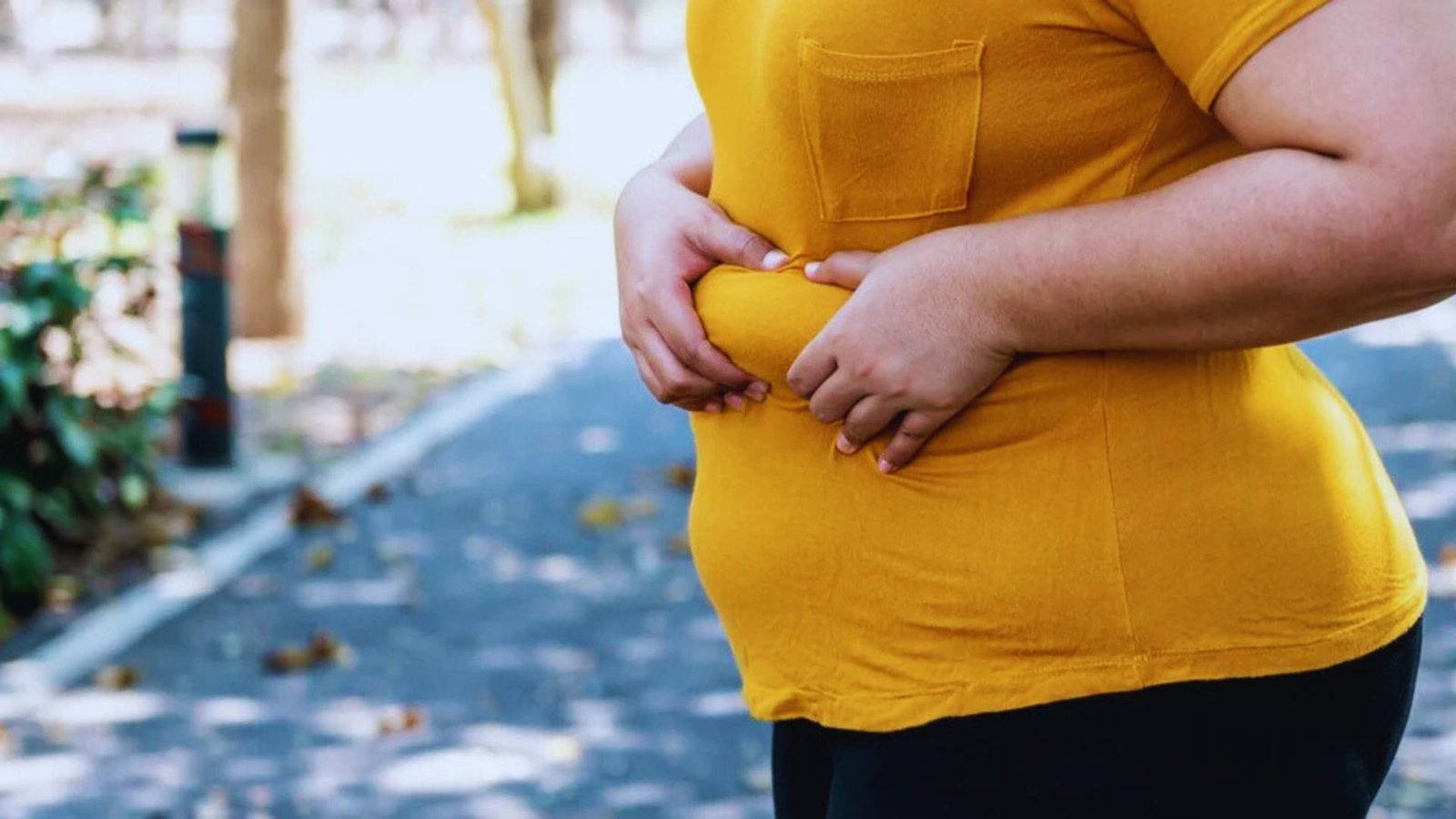 A woman stands with her hands resting on her stomach, conveying a sense of contemplation or comfort.