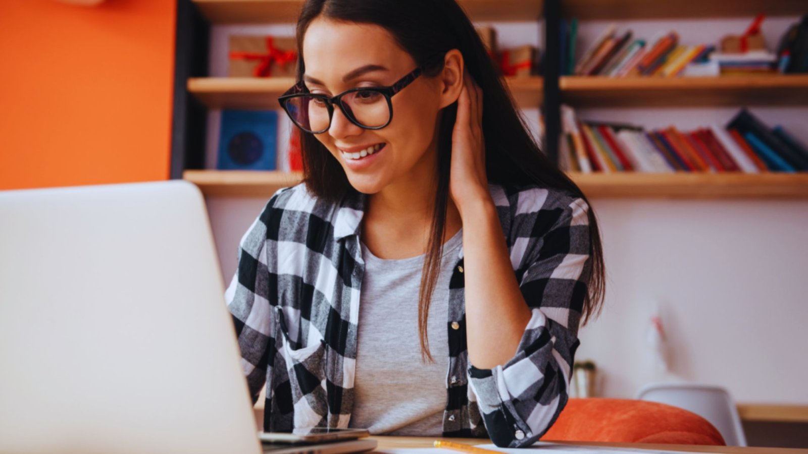  A woman wearing glasses smiles while working on her laptop, conveying a sense of joy and engagement.