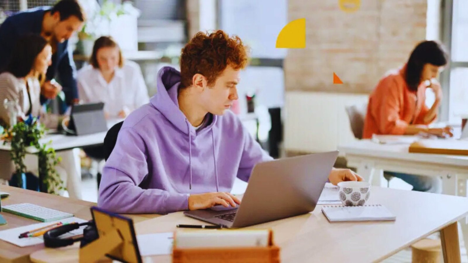 A man in a purple sweatshirt is focused on his laptop, working intently in a casual setting.
