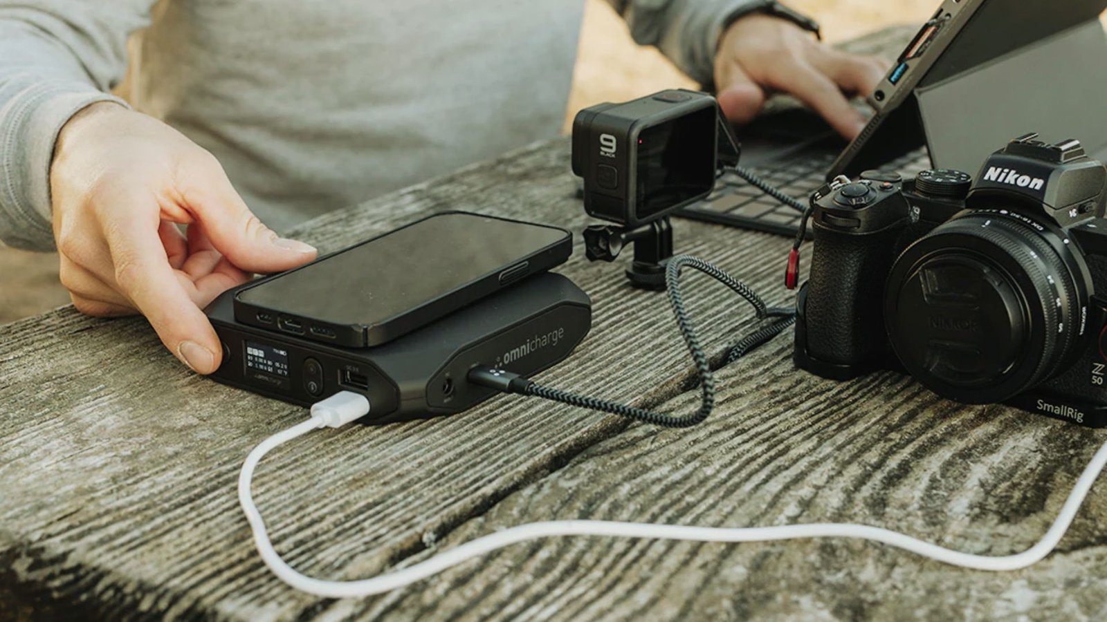 . A person holds a camera in one hand and a laptop on a table, ready to capture and edit images.