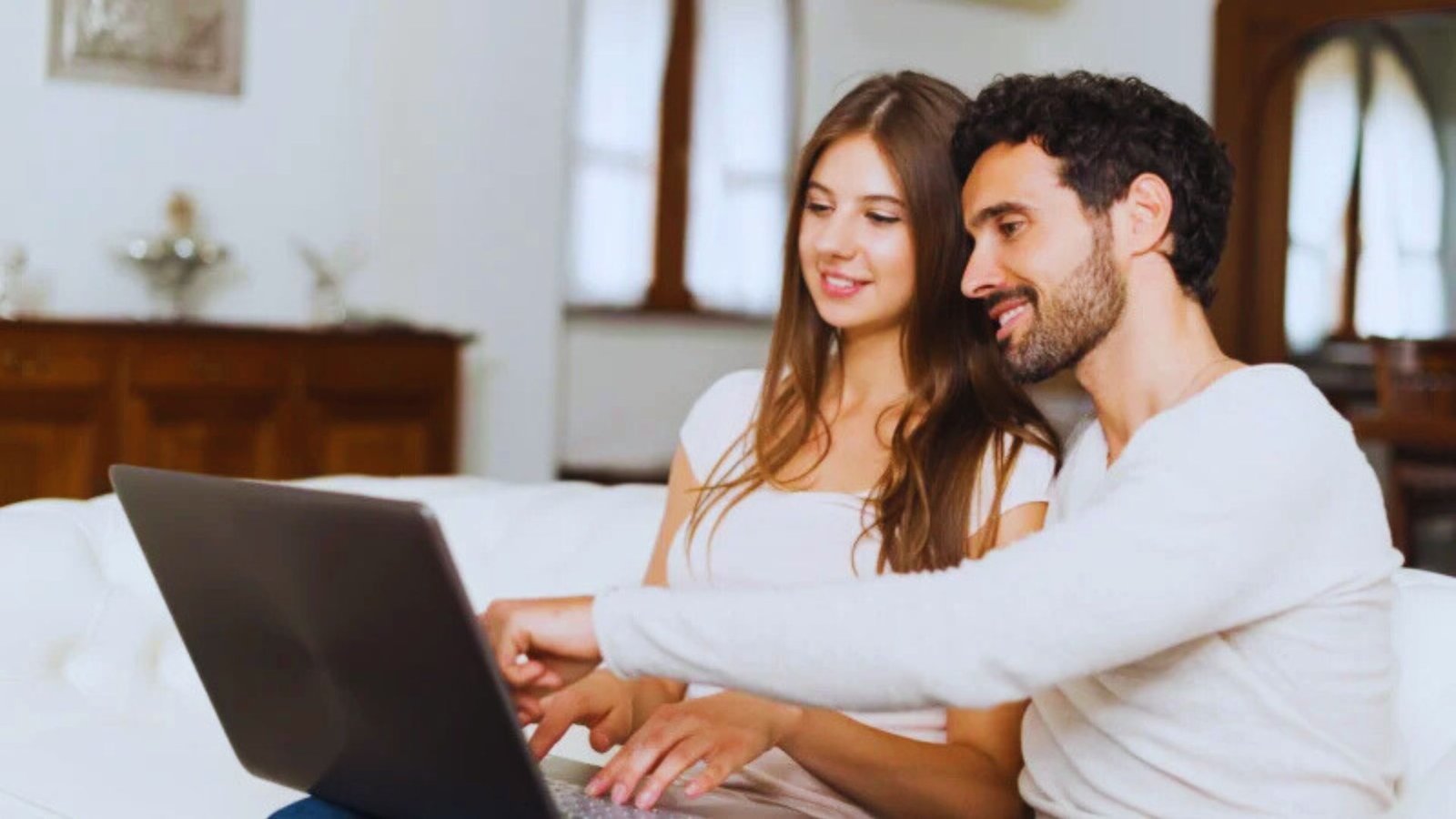  A man and woman sit on a couch, focused on a laptop screen between them.