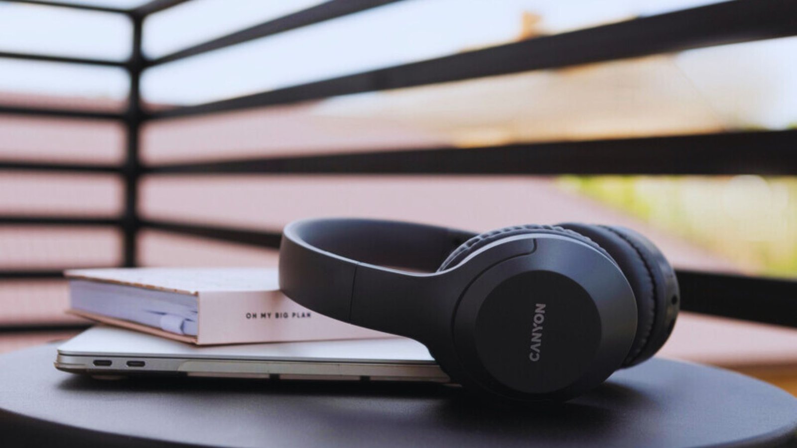 A pair of headphones rests on a table next to an open laptop, suggesting a workspace for listening or video calls.
