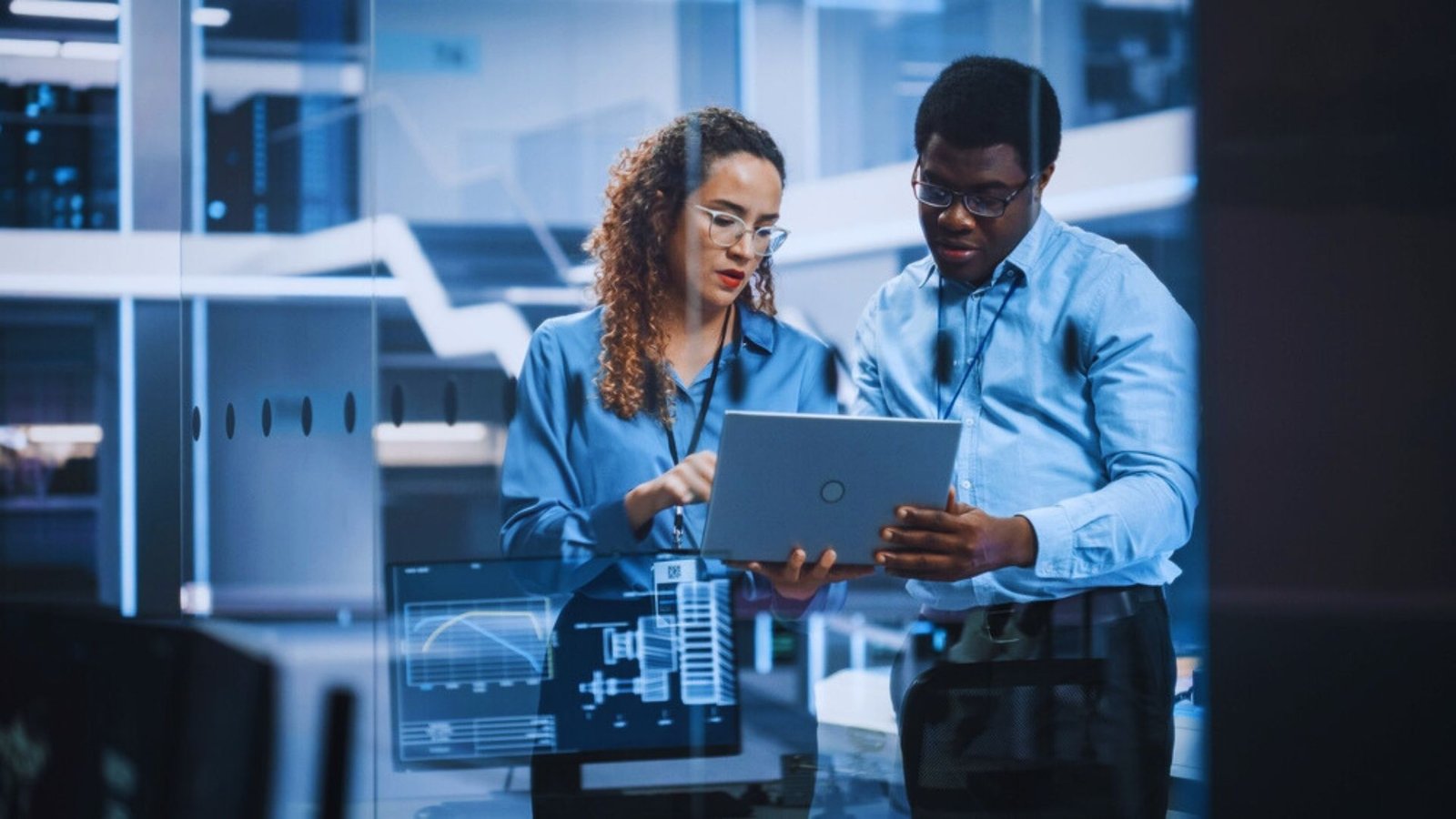 Two individuals examining a tablet computer together in a modern office setting.
