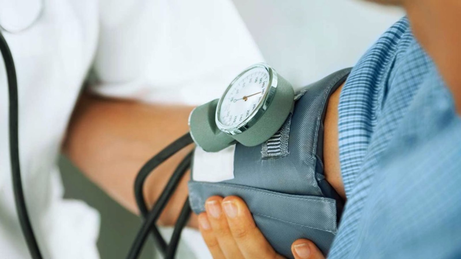 A doctor measures a patient's blood pressure using a sphygmomanometer in a clinical setting.