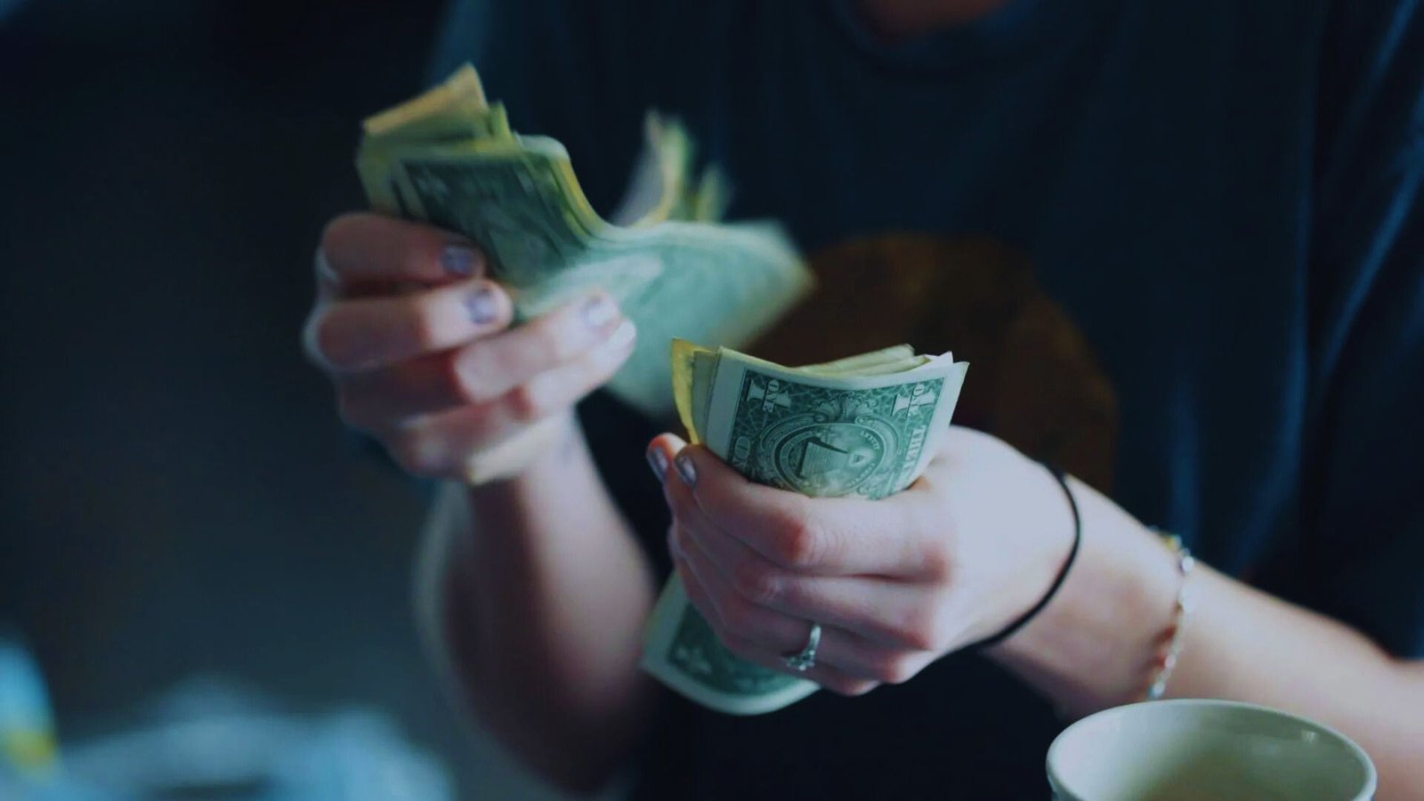 A person sitting at a table holds cash in their hand, looking focused on the money.