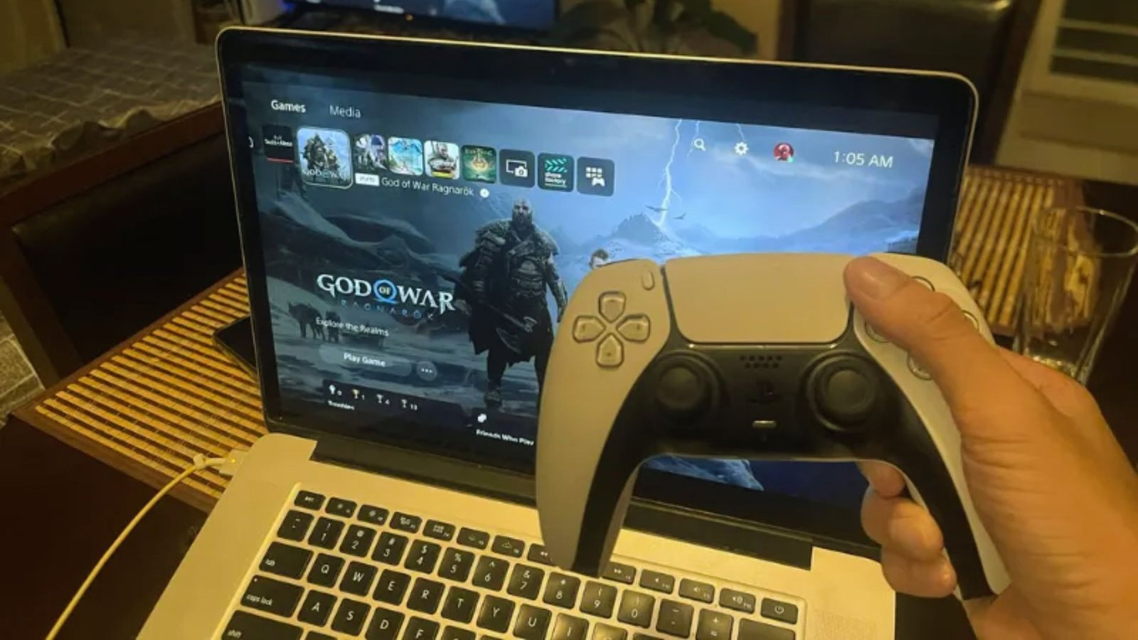 A person grips a gaming controller while seated in front of a laptop, focused on the screen.