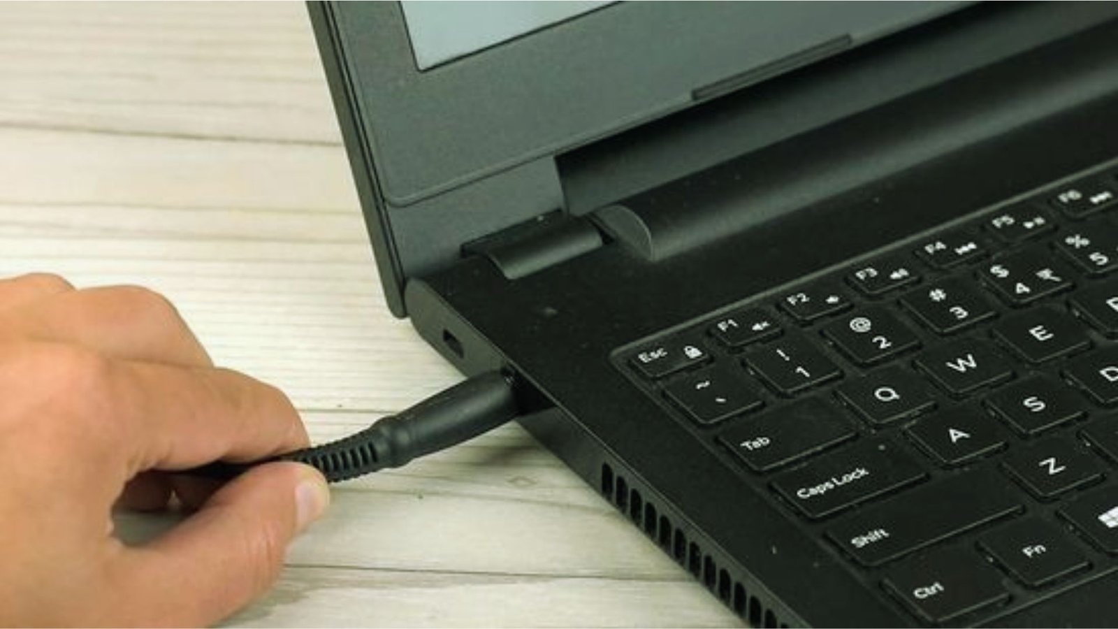 A person connects a laptop to a keyboard using a black cord.