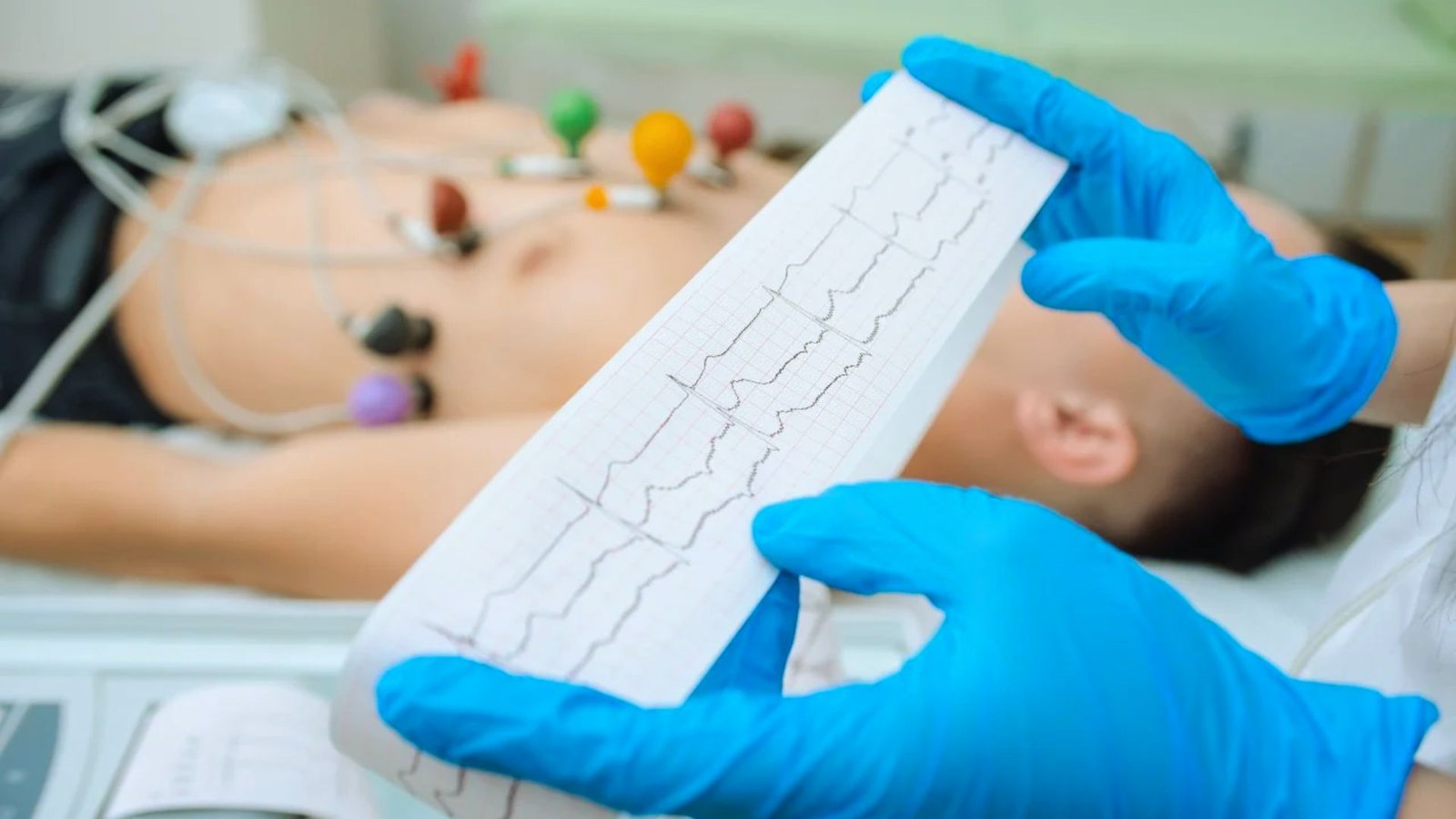. A person lies on a bed, connected to a heart monitor, indicating medical observation and care.