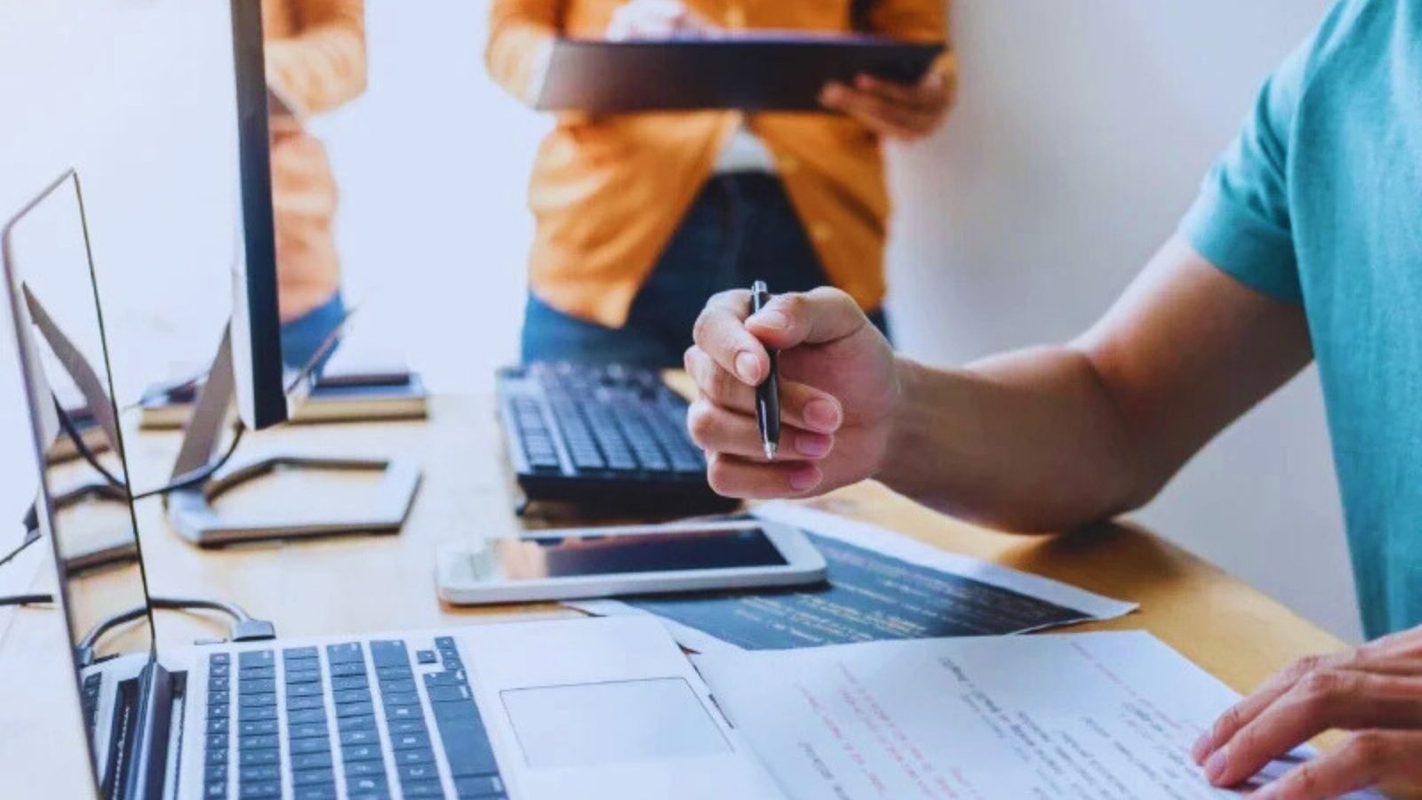  A man works on a laptop while another person sits behind him, observing the screen.