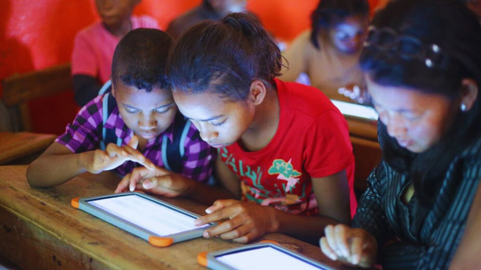  Children engaged with an iPad, focused on learning activities in a bright classroom setting.