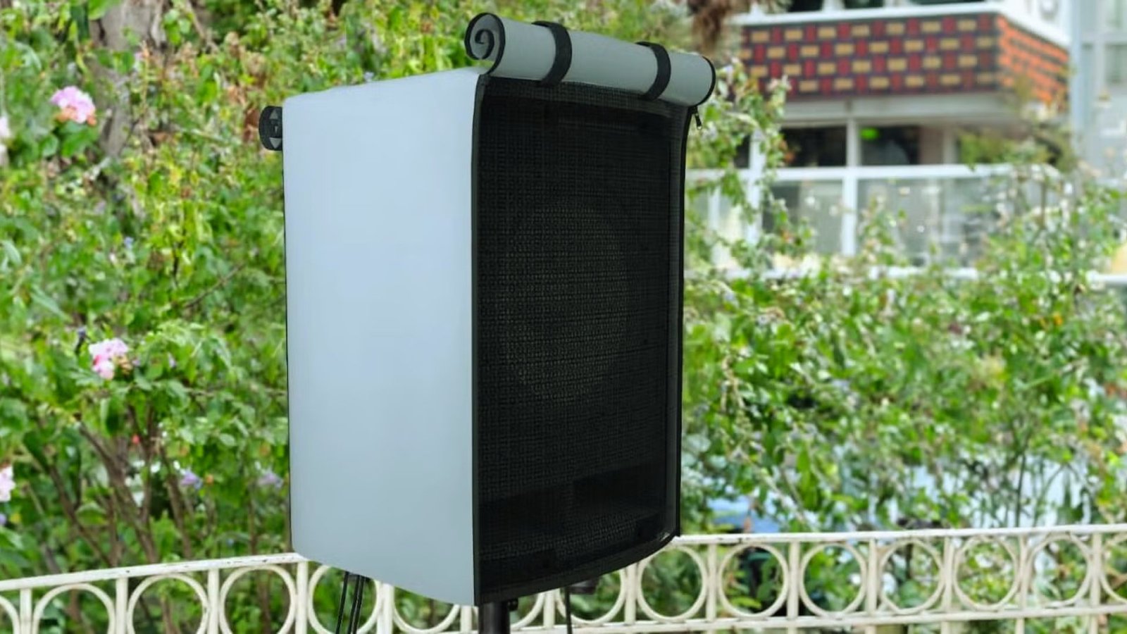 A speaker perched on a fence, overlooking a vibrant garden filled with various plants and flowers.
