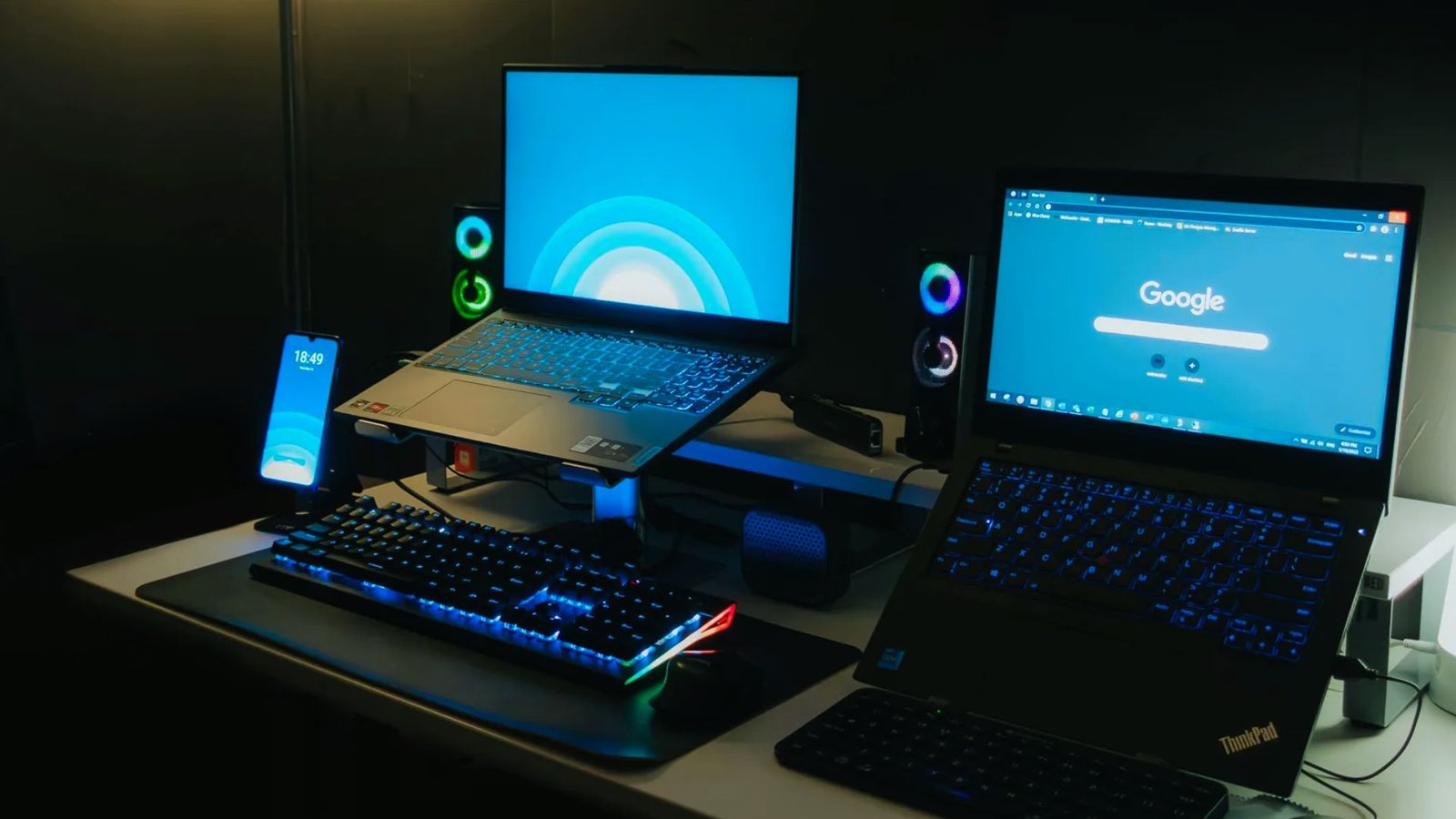 Two laptops and a keyboard are placed on a wooden desk, showcasing a workspace setup.
