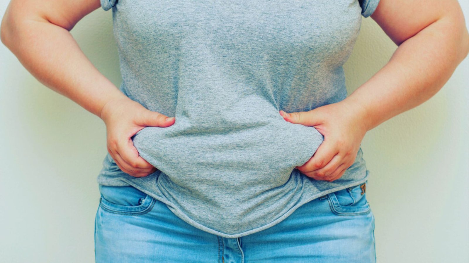 A woman stands with her hands resting on her stomach, conveying a sense of contemplation or comfort.