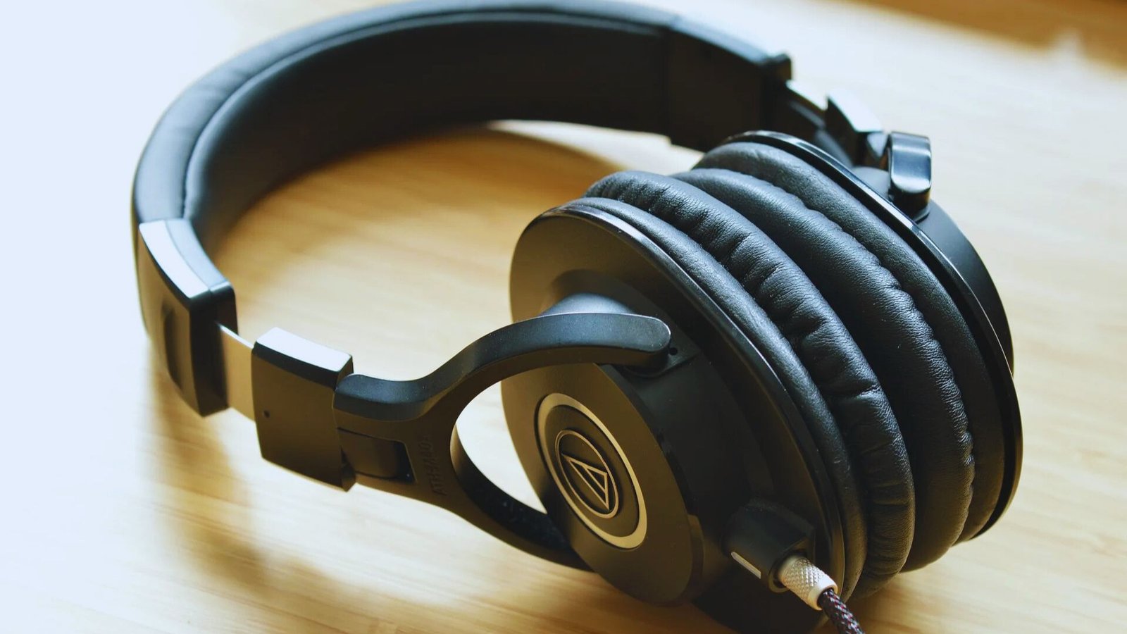 A pair of headphones resting on a wooden table, showcasing their sleek design against the natural wood grain.