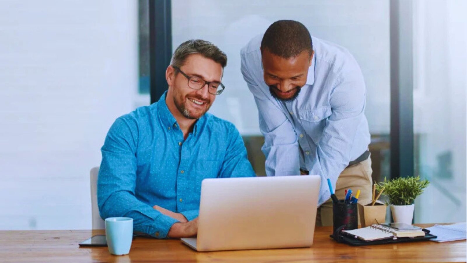 Two men collaborating on a laptop in a modern office setting, focused on their work.