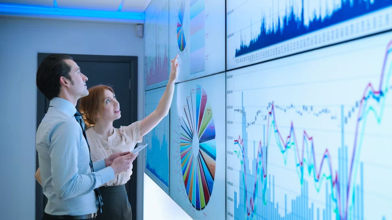 Two individuals analyzing data displayed on a large screen filled with various graphs and charts.