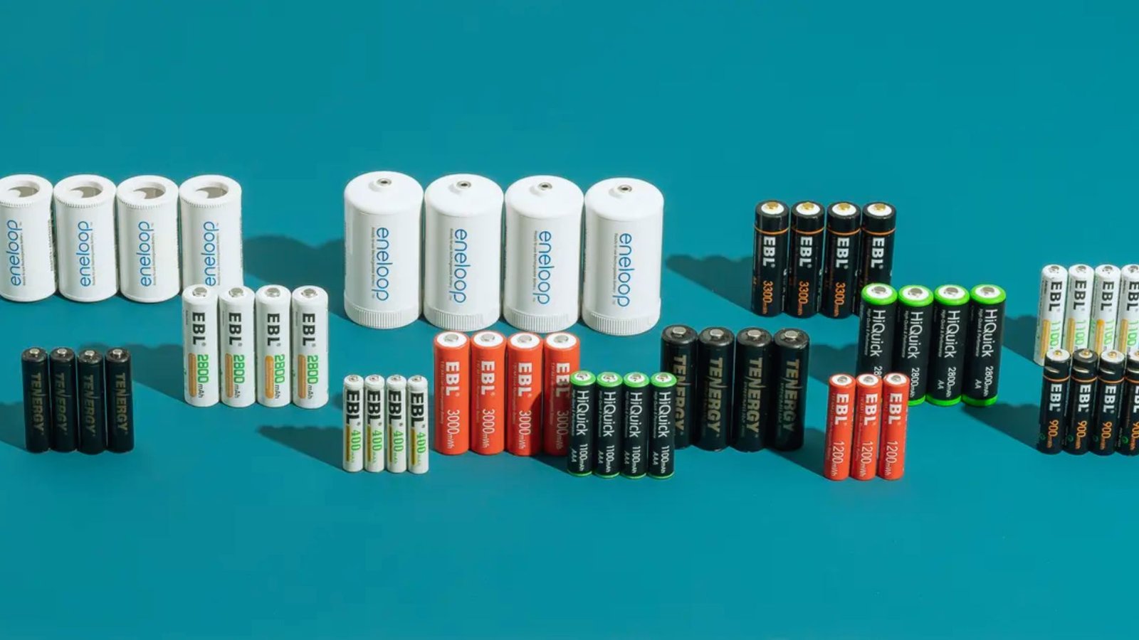  A variety of batteries and chargers arranged on a blue surface, showcasing different sizes and types.
