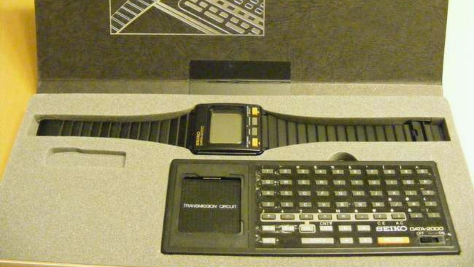 A watch and a keyboard neatly arranged inside a box, showcasing their design and functionality.
