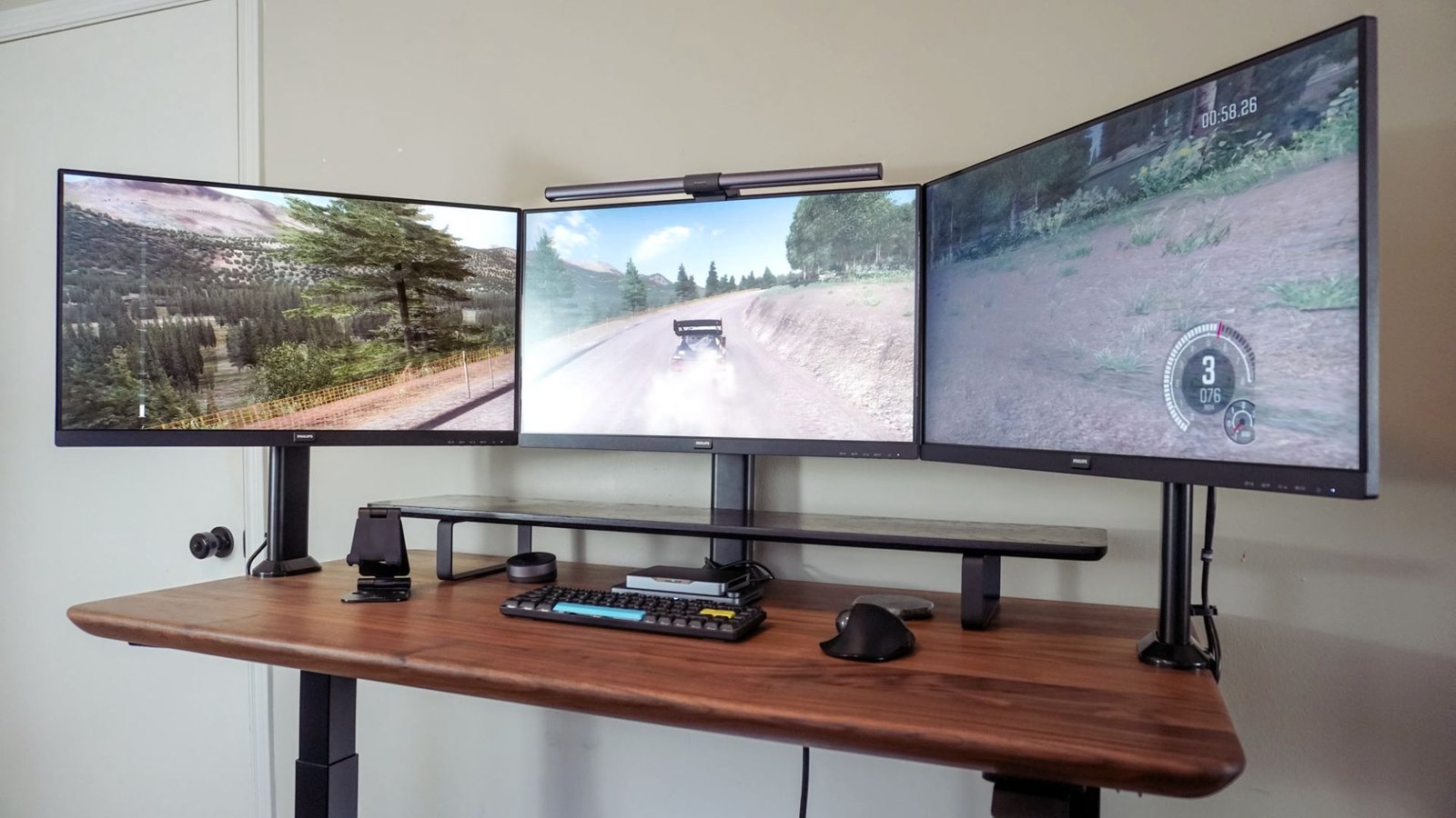 Three monitors on a sleek wooden desk display a racing game with a car driving on a dirt road. The setup conveys a modern, immersive gaming experience.