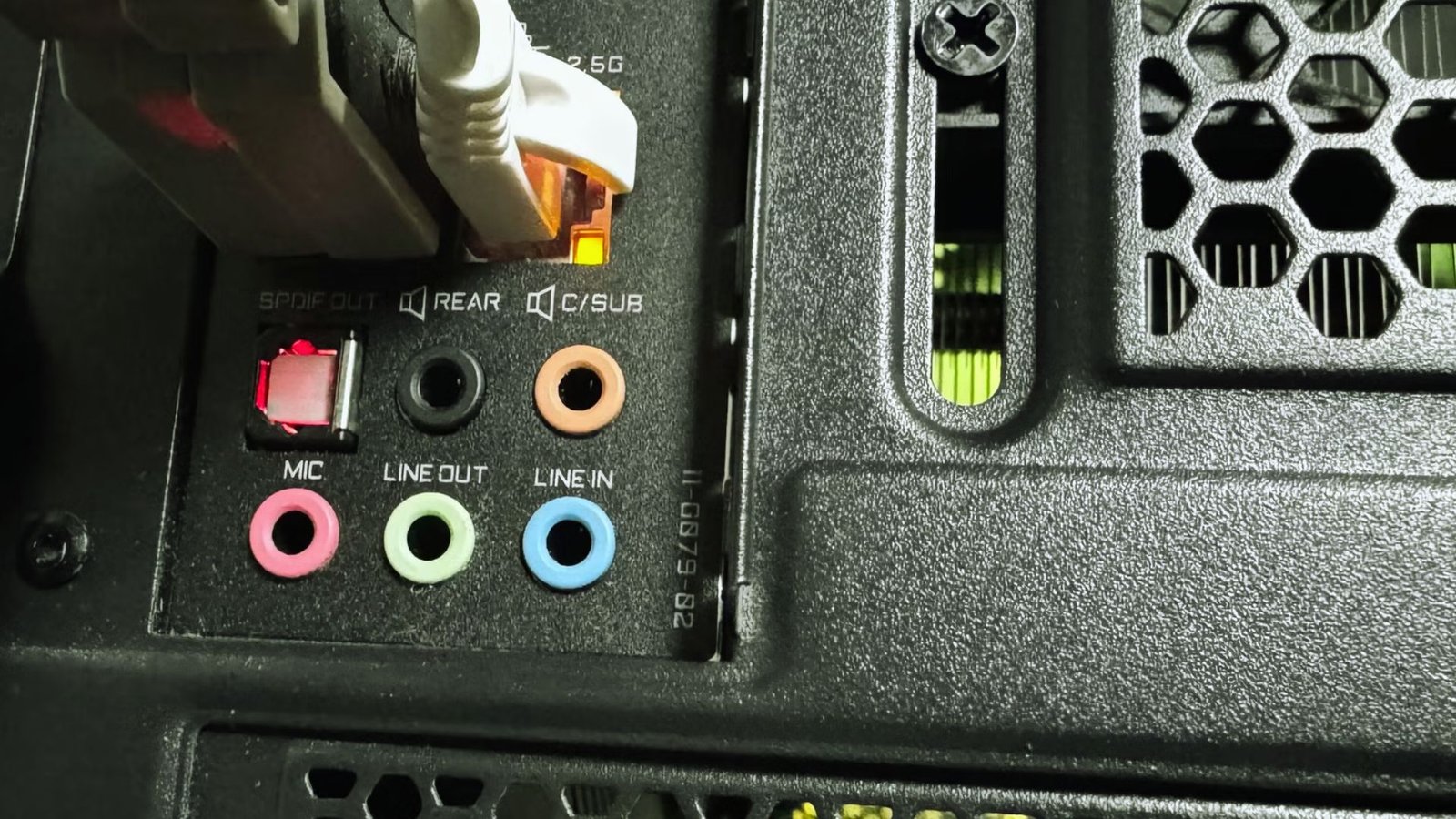 Close-up of a computer back panel showing ethernet, audio ports, and a grid vent. Cables are plugged in, with colorful audio jacks visible.